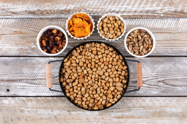 Combien de grammes de croquette par jour pour un chat ? - top view different kind snacks as nuts crackers cookies bowls white wooden surface horizontal Portions croquettes pour chat